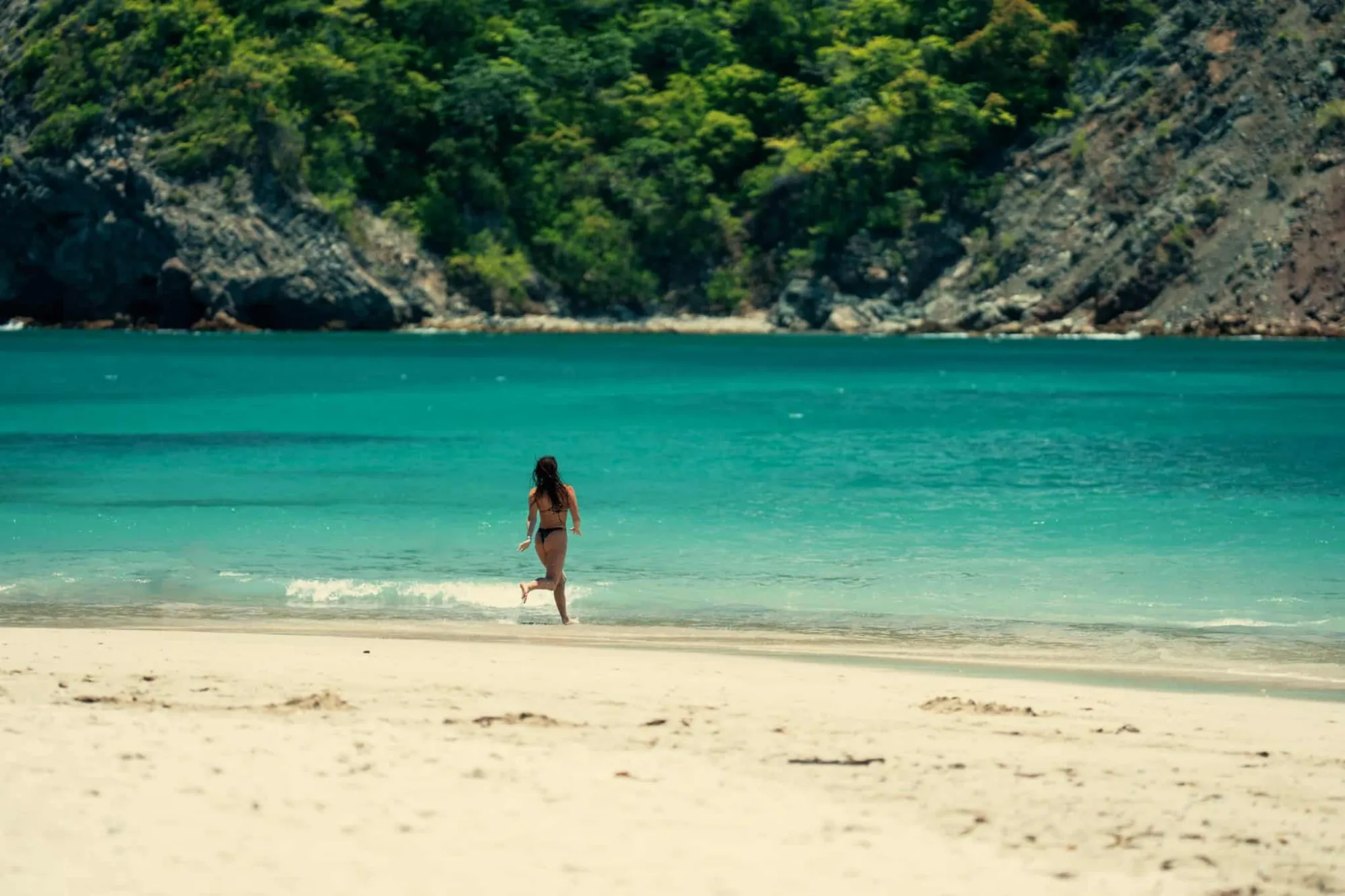 A guest running into the turquoise water from a white sand beach